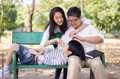 Happy Asian family and relaxing on the bench together in the public park. The concept of lifestyle in the family holiday