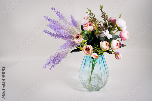 A bouquet of roses with lavender in a transparent glass vase on a gray-violet background. Front view