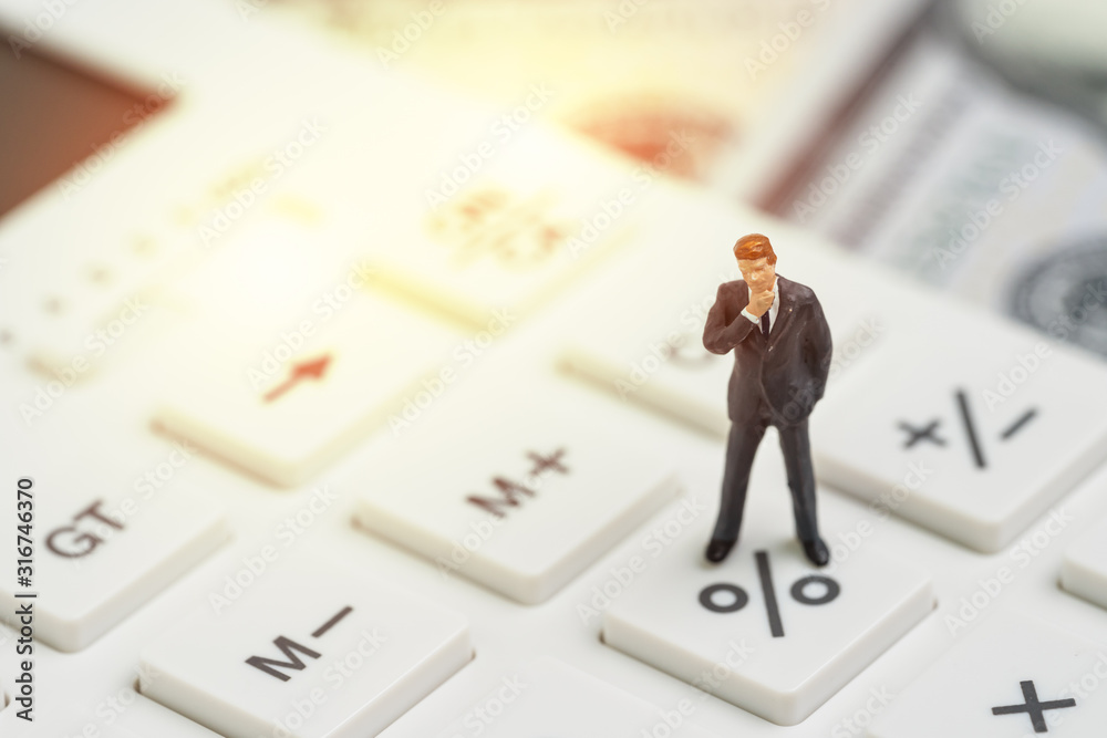 Miniature people business man standing and thinking on calculator percentage button with background of US Dollar banknote using as FED consider interest rate, business profit or stock market analyst Miniature people business man standing and thinking on calculator percentage button with background of US Dollar banknote using as FED consider interest rate, business profit or stock market analyst