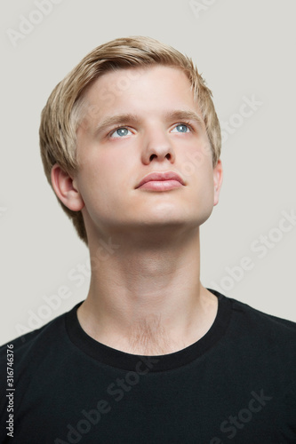Contemplative young man looking up against gray background