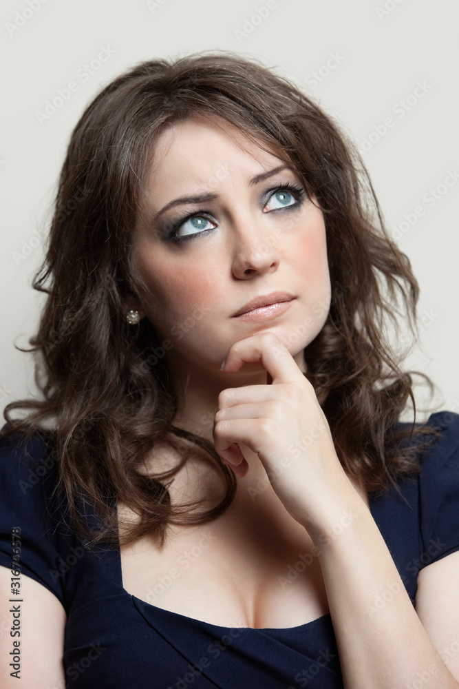 Contemplative young woman looking up against gray background Contemplative young woman looking up against gray background