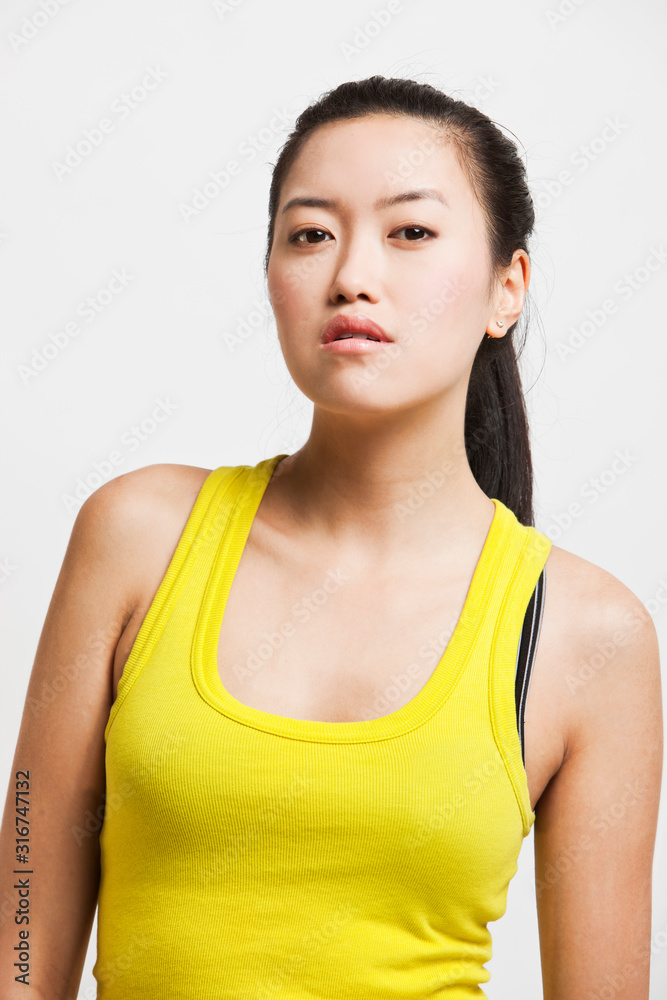 Portrait of confident young woman in yellow tank top against white background Portrait of confident young woman in yellow tank top against white background
