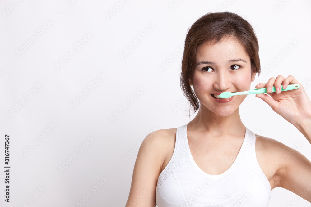 Young Asian woman in white tank top brushing teeth against white background Young Asian woman in white tank top brushing teeth against white background