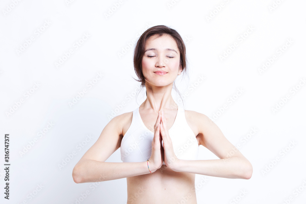 Young Asian woman in white sports bra meditating against white background Young Asian woman in white sports bra meditating against white background