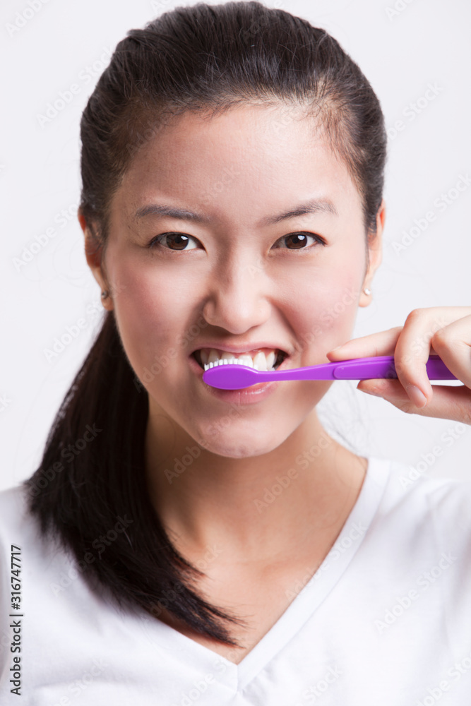 Portrait of young woman brushing her teeth against white background Portrait of young woman brushing her teeth against white background