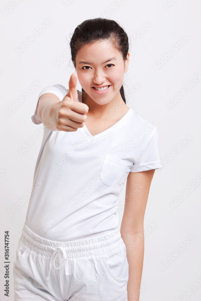 Portrait of young Asian woman gesturing thumbs up against white background Portrait of young Asian woman gesturing thumbs up against white background