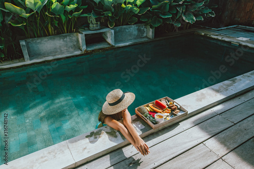 Fotografia Girl relaxing and eating fruits in the pool on luxury villa in Bali