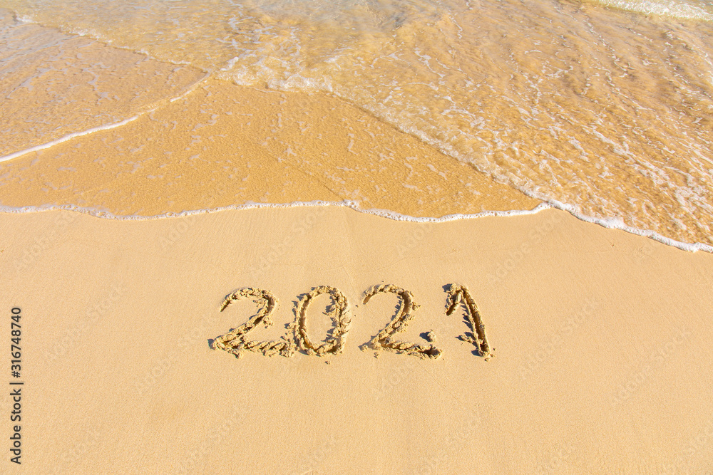 Fototapeta premium New Year 2021 is coming - inscription 2021 on a beach sand, the wave is starting to cover the digits - Summer beach holiday 2021 season golden sand - old year - message handwritten - empty copy space