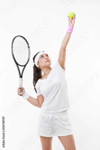 Young female tennis player preparing to serve ball against white background