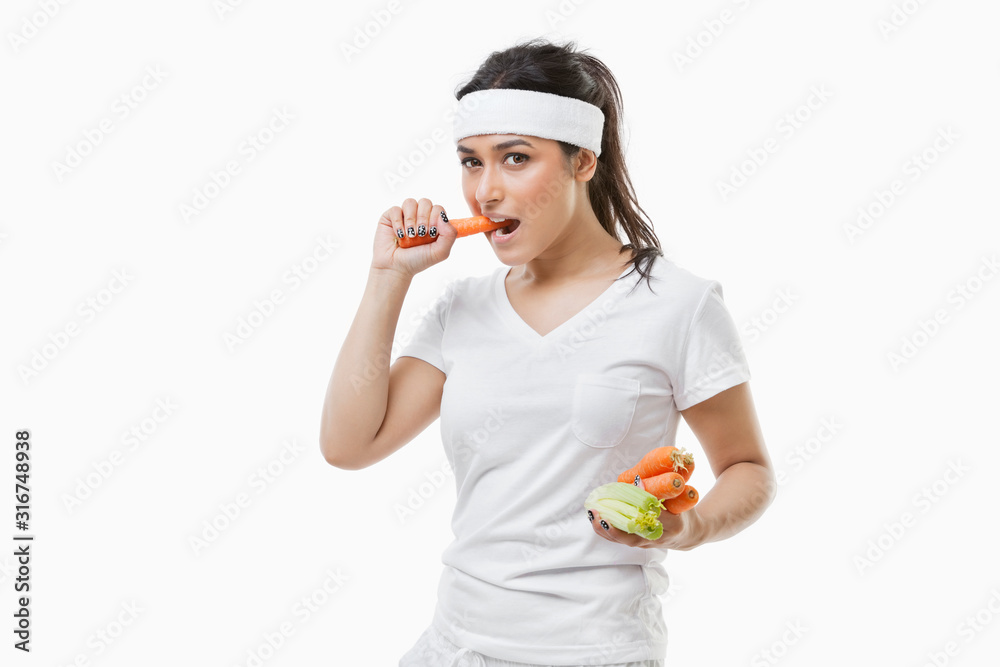Portrait of young sportswoman eating carrot over white background Portrait of young sportswoman eating carrot over white background