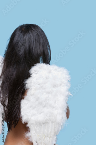 Back view of young woman wearing artificial wings over blue background