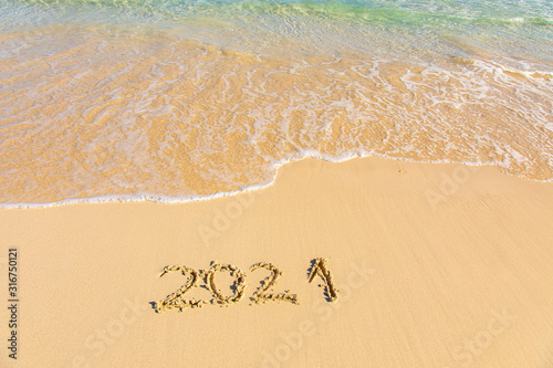 New Year 2021 is coming - inscription 2021 on a beach sand, the wave is starting to cover the digits - Summer beach holiday 2021 season golden sand - old year - message handwritten - empty copy space