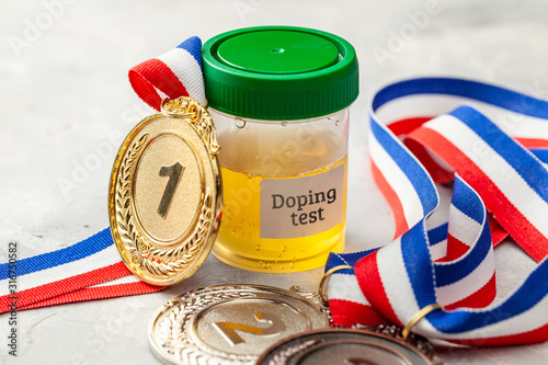 Doping test. Gold, silver and bronze medal and a jar for urine analysis on a gray background