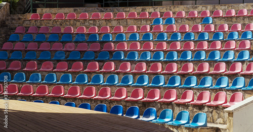 Empty auditorium in the open. Semicircular plastic chairs are arranged in rows from bottom to top.  Colorful theater background.
