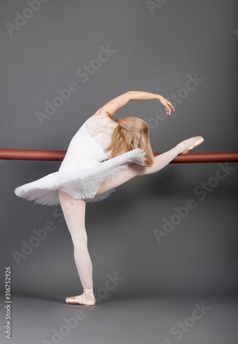 Fototapeta Naklejka Na Ścianę i Meble -  Young female ballet dancer stretching at ballet bar over grey background