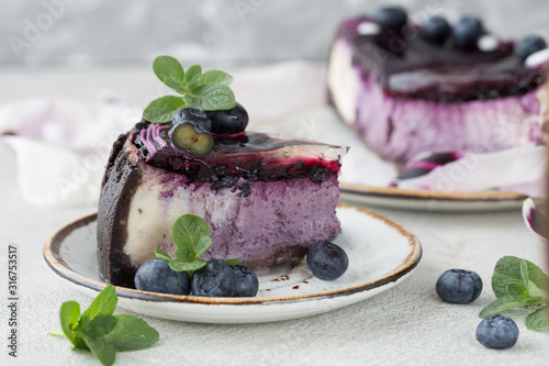 Slice of Blueberry flavour cheesecake swirled with blueberry sauce on a  biscuit crumb  bakery. Delicious slice of blueberries cheesecake with  jam and green mint.  Sweet and tasty food  coffee break 