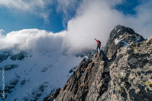 An alpinist standing on top of a high rock and watching winter mountain alpine landscape. Hiker or climber on an adventure ascent to the summit of an alpine peak. Mountainer celebrating success.