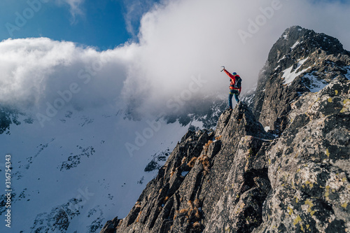 An alpinist standing on top of a high rock and watching winter mountain alpine landscape. Hiker or climber on an adventure ascent to the summit of an alpine peak. Mountainer celebrating success.