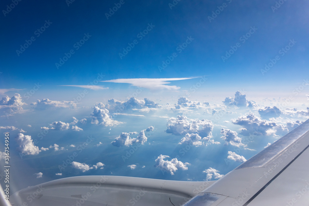 Airplane wing above fluffy white clouds in a blue sky.