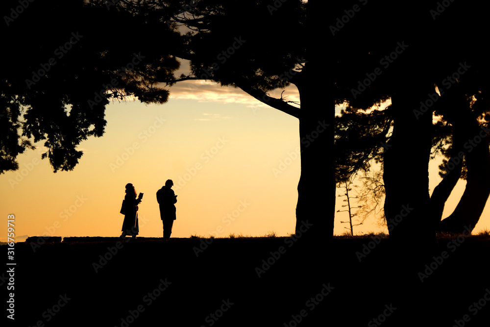 Silhouettes of unrecognizable people enjoying the sunset in Sustipan park in Split, Croatia.