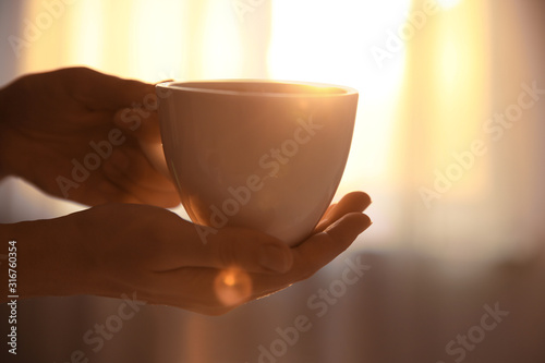 Woman holding cup of drink on blurred background, closeup. Lazy morning