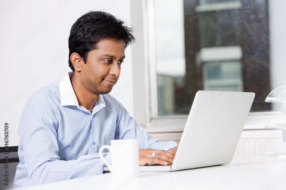 Young businessman using laptop at desk in office Young businessman using laptop at desk in office