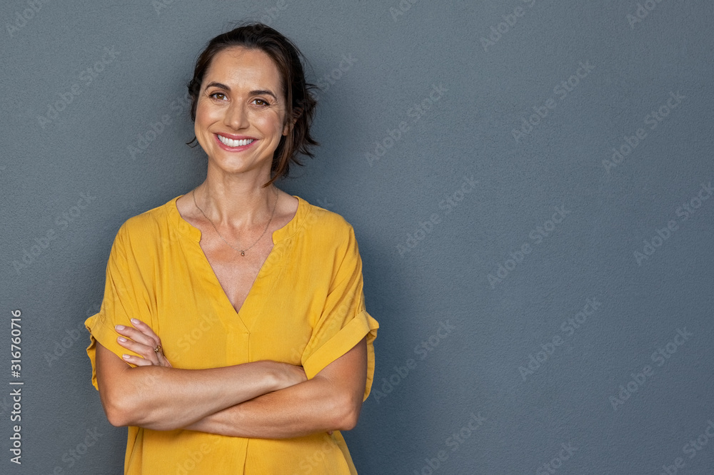 Happy mature woman smiling on grey wall - obrazy, fototapety, plakaty 