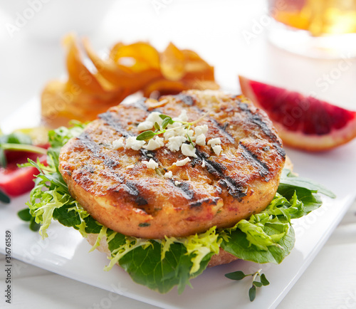 Closeup of open face fish patty sandwich sitting on top of lettuse with a side of tomatos and potato chips photo