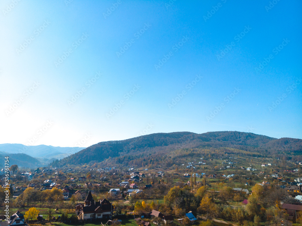 Aerial view of the small village of Sheshory, surrounded by the Carpathian mountains. Buildings and infrastructure. The nature of Ukraine. Sunny autumn day. Huk waterfall on the Pistynka River.