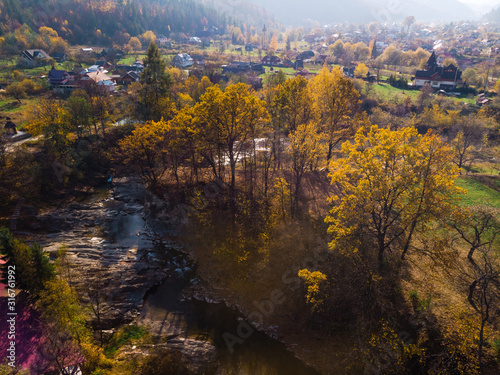 Fototapeta Naklejka Na Ścianę i Meble -  Aerial view of the small village of Sheshory, surrounded by the Carpathian mountains. Buildings and infrastructure. The nature of Ukraine. Sunny autumn day. Huk waterfall on the Pistynka River.