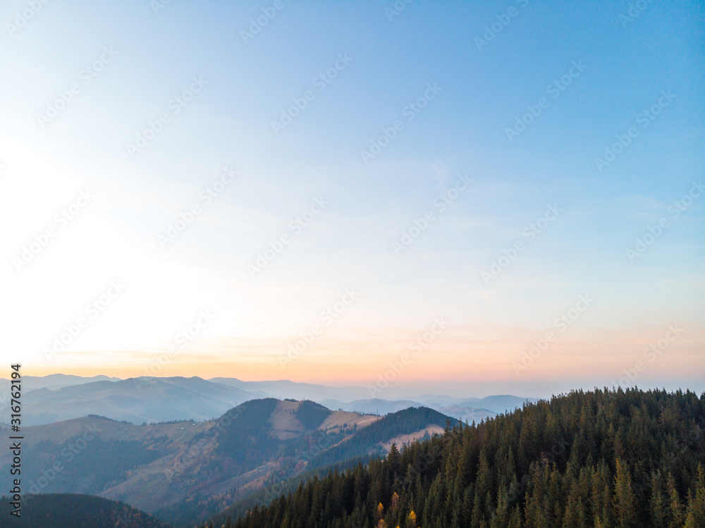 Aerial view of the Carpathian mountains in autumn. Pine forest, houses on the peaks, yellow fields and trees. Mountain meadow. sunset, Ukraine, Europe