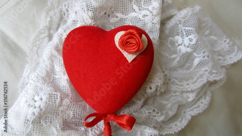 A red heart on a stick with a small red bow, decorated with a small red rose, lying on white lace panties. Saint Valentine's Day gift concept. 