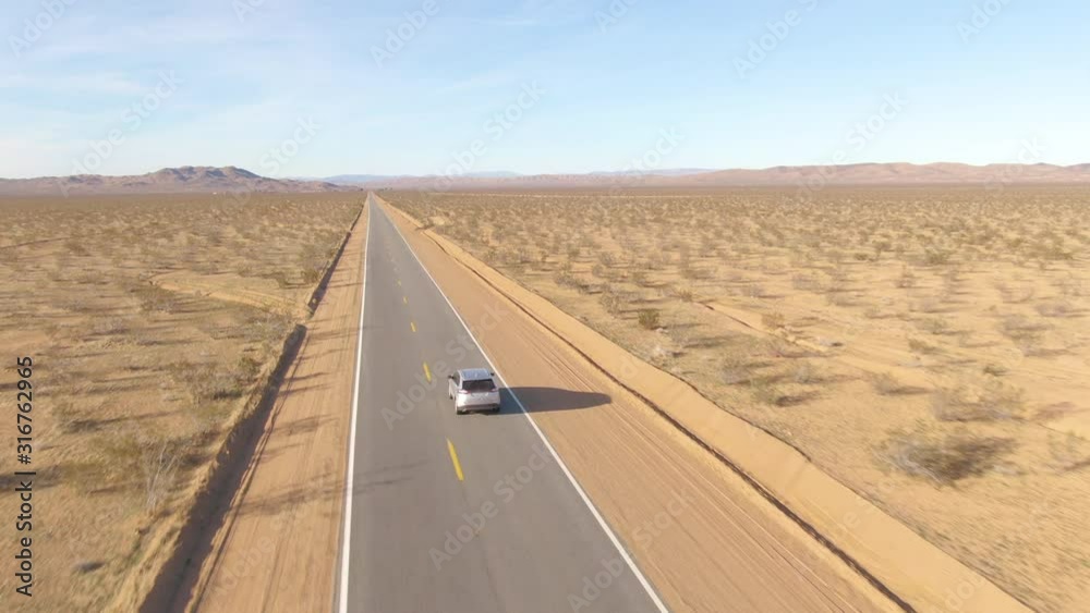 DRONE Barren landscape surrounds a silver SUV driving down an empty