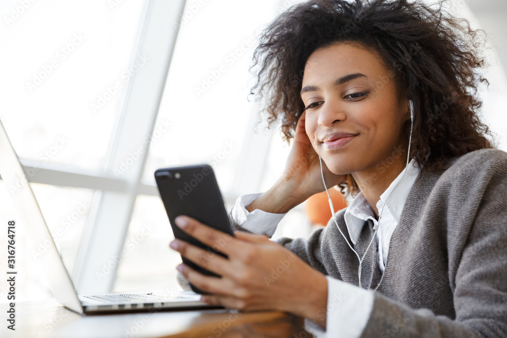 Portrait of young woman using laptop and cellphone while sitting by window
