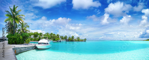 White Boat at pier with palm trees  Maldives island. Beautiful panoramic tropical landscape with turquoise ocean and blue sky with clouds.