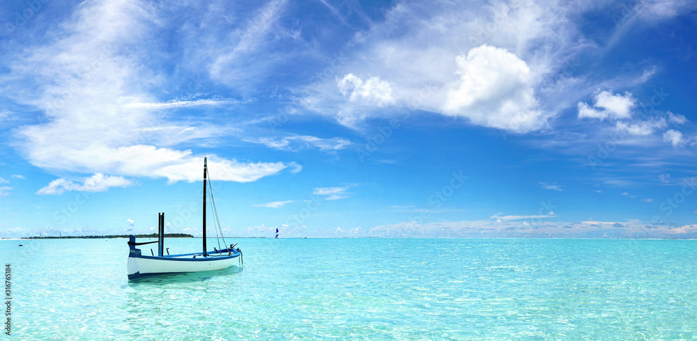 Boat in turquoise ocean water against blue sky with white clouds. Natural landscape for summer vacation.