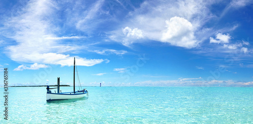 Boat in turquoise ocean water against blue sky with white clouds. Natural landscape for summer vacation.