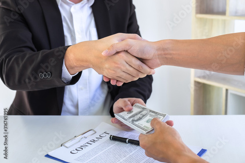 Businessman handshake with money of dollar banknotes in hands from money of their partner to give success the deal contract in a corruption scam, illegal, dishonest, bribery and corruption concept