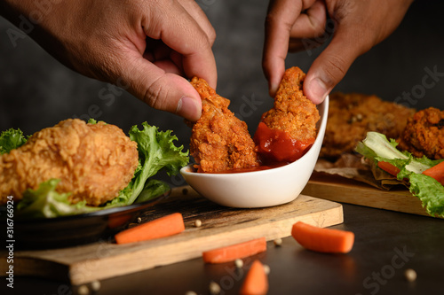 Two hand holding crispy fried chicken dipped in tomato sauce photo