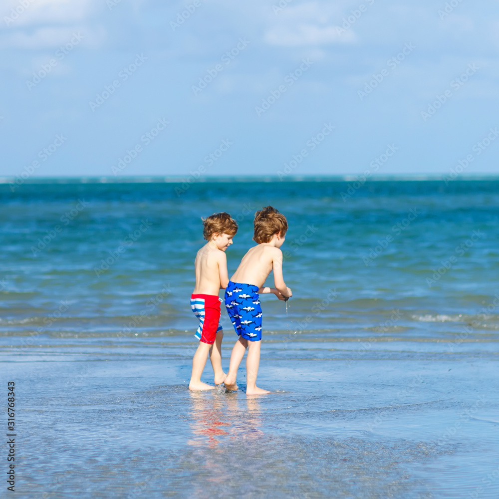 Two little kids boys having fun on tropical beach, happy best friends playing, friendship concept. Siblings brothers, twins in family look with palms on background. Family vacations on ocean. Two little kids boys having fun on tropical beach, happy best friends playing, friendship concept. Siblings brothers, twins in family look with palms on background. Family vacations on ocean.