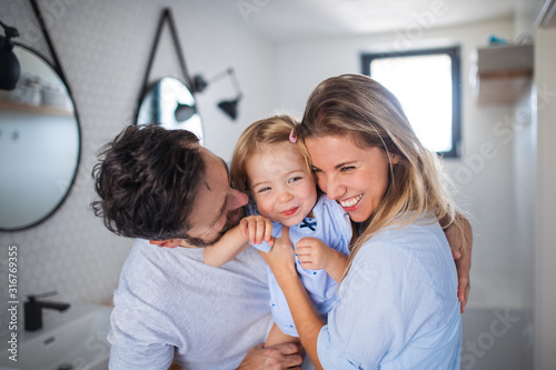 Fotografiet Young family with small daughter indoors in bathroom, hugging.