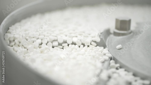 White pills moving on metal automatic line in workshop of pharmaceutical factory. Closeup view of drugs move along conveyor belt during work process in pharma chemical company. Concept: business