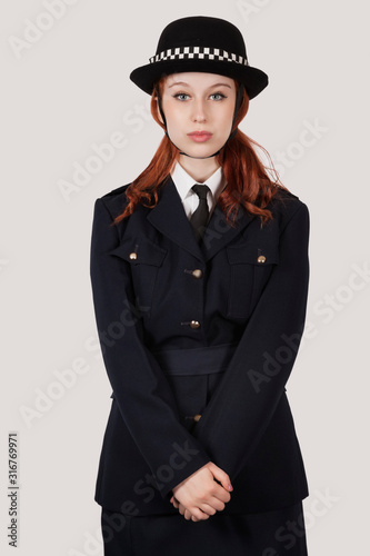 Portrait of young woman in police officer's costume standing against gray background