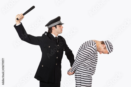 Side view of police officer with nightstick arresting male prisoner against gray background photo