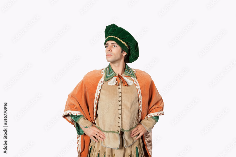Thoughtful young man in old-fashioned costume with hands on hips against gray background Thoughtful young man in old-fashioned costume with hands on hips against gray background