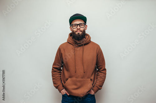 Handsome hipster guy with beard wearing brown blank hoodie or hoody and black cap with space for your logo or design on white background. Mockup for print photo