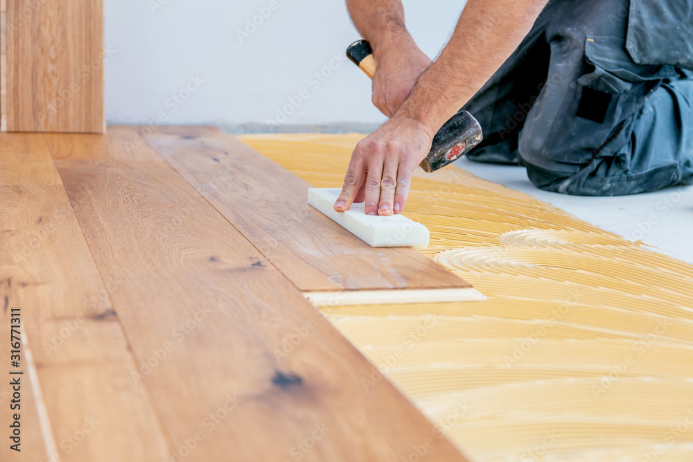 Craftsman is laying parquet flooring in a modern new building Craftsman is laying parquet flooring in a modern new building