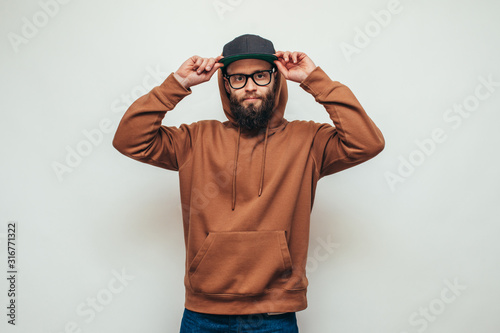 Handsome hipster guy with beard wearing brown blank hoodie or hoody and black cap with space for your logo or design on white background. Mockup for print