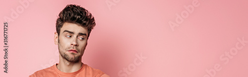 panoramic shot of offended young man looking away on pink background
