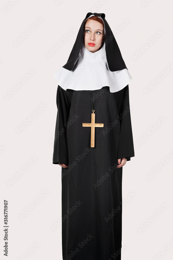 Young woman with in nun costume standing against gray background